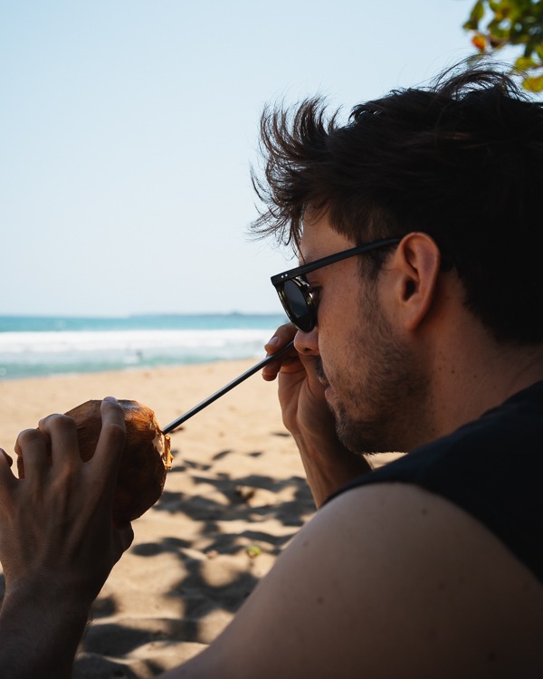 ein Mann am Strand mit einer Kokosnuss