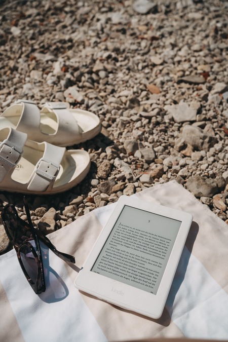 Pebble beach with a towel, a Kindle, and a pair of Birkenstocks