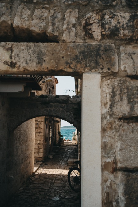 2 people by the sea in Prvić Luka, photographed through a small house facade