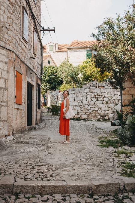 A young woman looks into the camera while standing in an alley in Prvić Luka, Croatia.